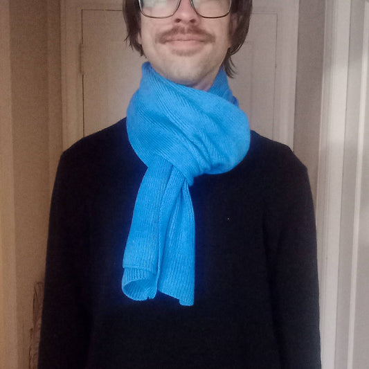 Person wearing a bright blue scarf and black sweater indoors.