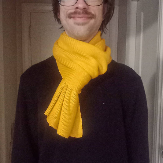 Person wearing a yellow scarf and dark sweater indoors.