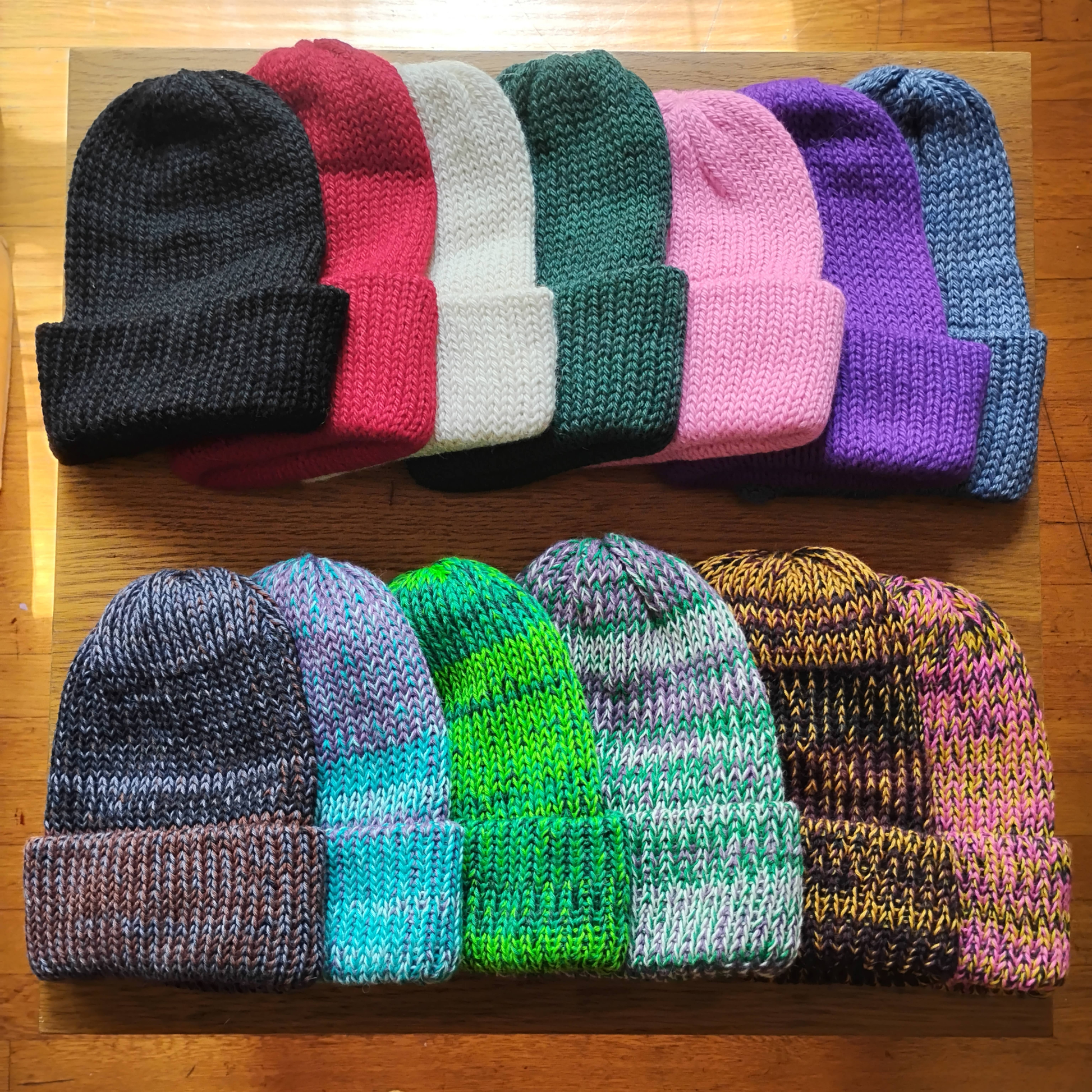 Knit baby alpaca beanies in various colors and patterns, arranged in two rows on a wooden surface.