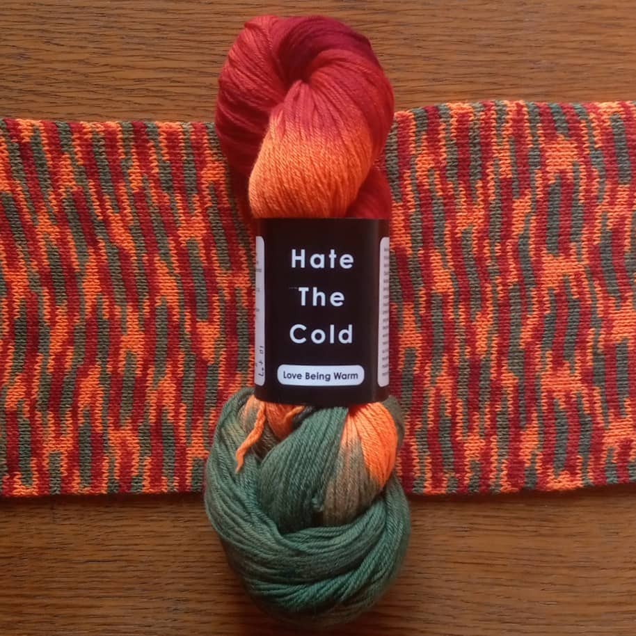 A skein of variegated merino wool yarn in red, orange, and green with a scarf knit from that yarn.