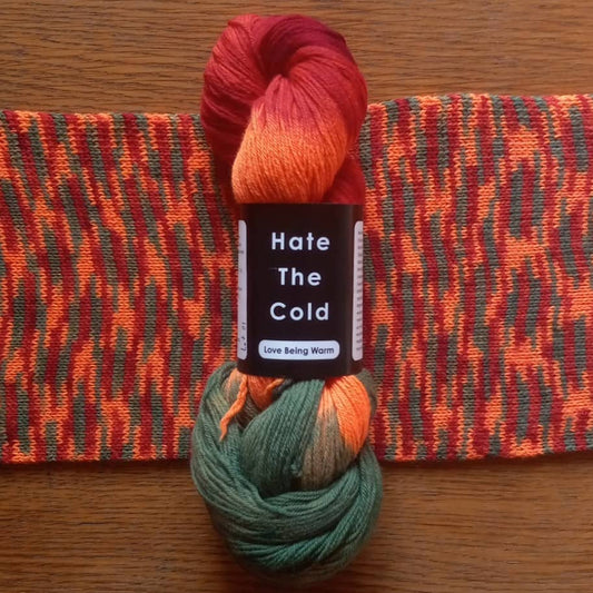 A skein of variegated merino wool yarn in red, orange, and green with a scarf knit from that yarn.