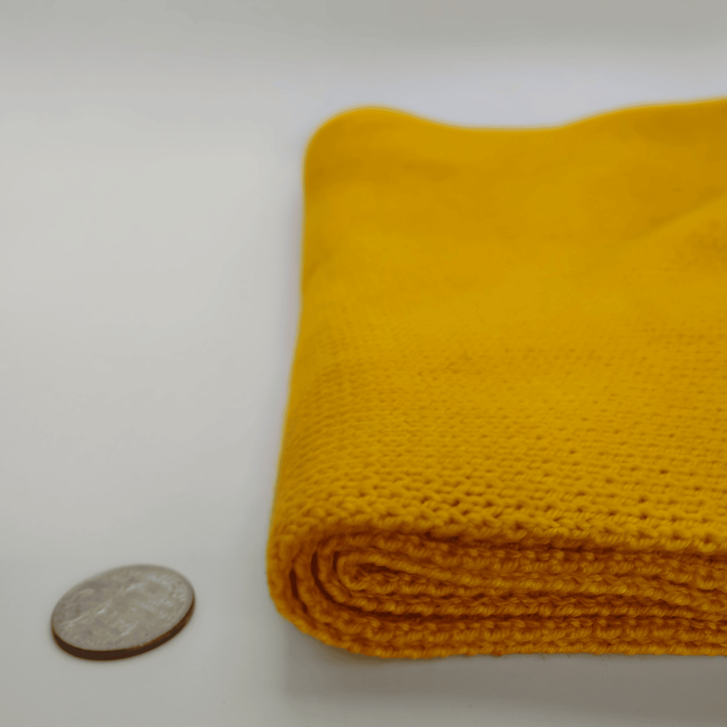 A folded dark green merino wool scarf shown on a white background next to a coin for scale.